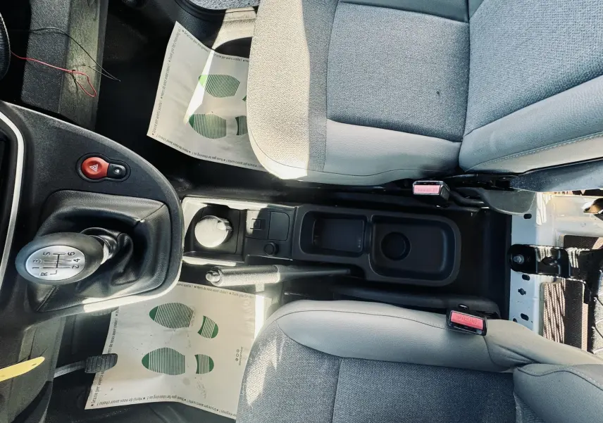 Vue intérieure centrée sur la console centrale et levier de vitesses manuelle du Renault Kangoo blanc, sièges gris.