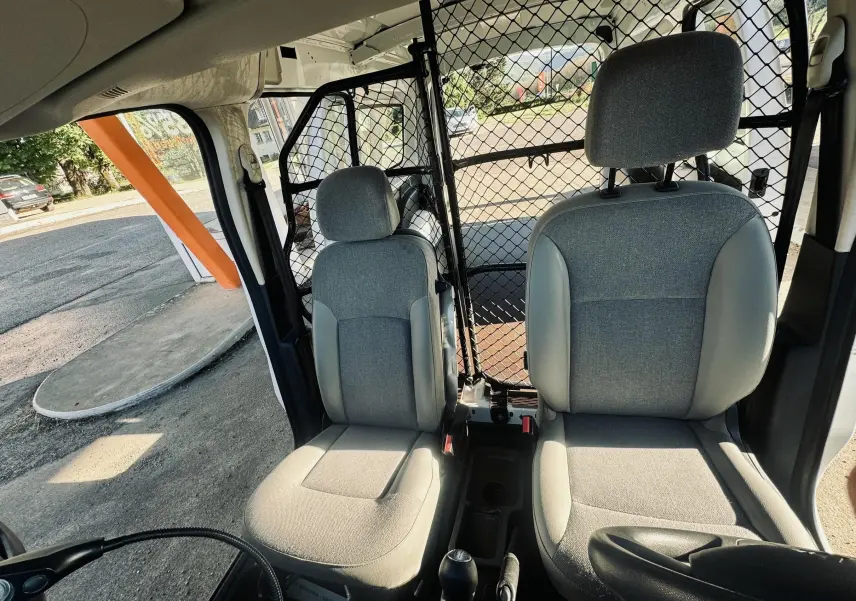 Vue intérieure avant du Renault Kangoo Maxi blanc, sièges gris avec séparation grillagée entre cabine et espace arrière.