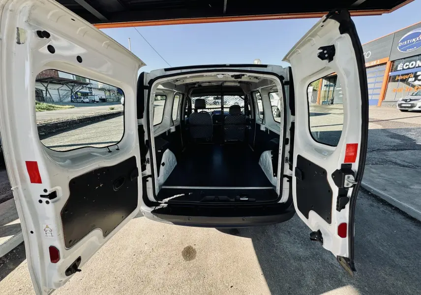 Vue arrière du Renault Kangoo blanc avec portes ouvertes montrant l'espace de chargement vide et la cloison métallique.