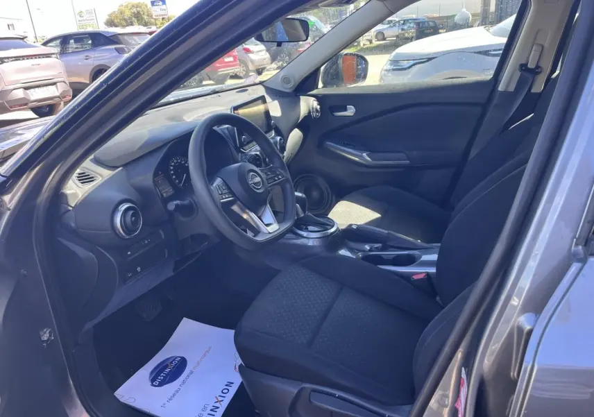 Intérieur avant droit du Nissan Juke 2023 gris Argile, sièges tissu noir et tableau de bord avec écran tactile.