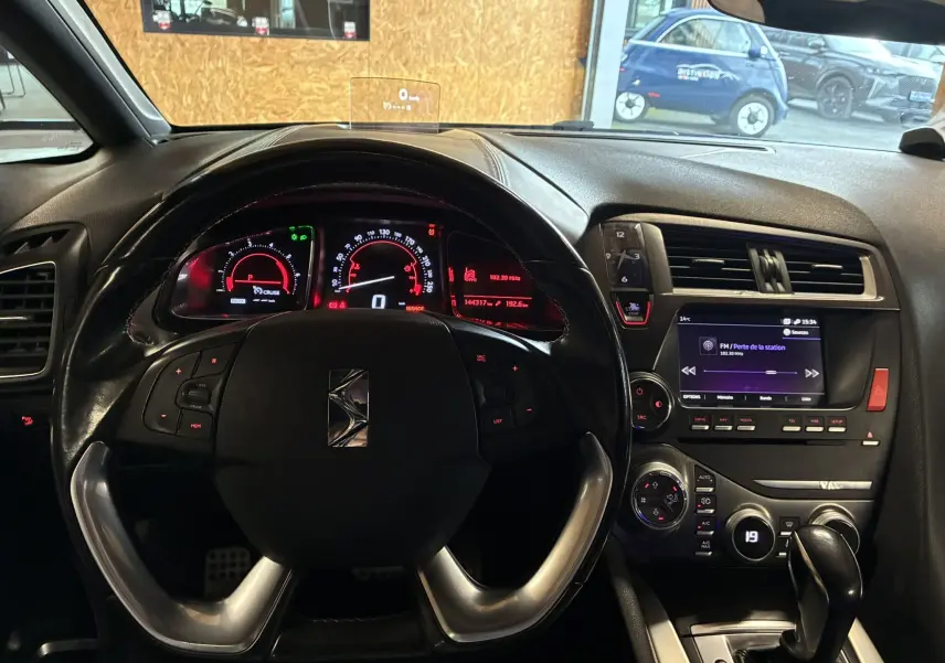 Vue intérieure centrée sur le volant noir et le tableau de bord lumineux du DS5 gris, avec écran multimédia et commandes visibles.