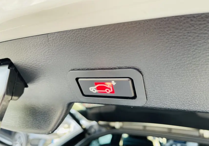 Bouton d'ouverture électrique du coffre vu de dessous dans un BMW X6 blanc, intérieur noir.