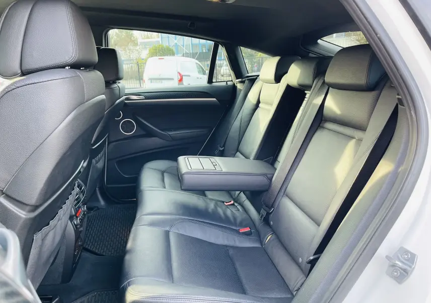 Vue intérieure côté droit des sièges arrière en cuir noir d'un BMW X6 blanc, avec accoudoir central déployé.