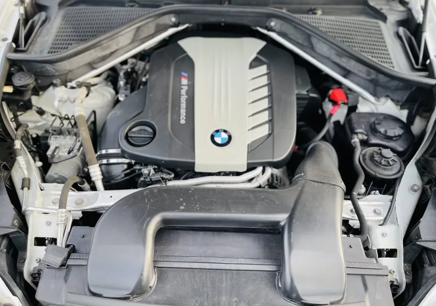 Vue rapprochée du moteur M Performance d’un BMW X6 blanc 50D, montrant le compartiment moteur ouvert.