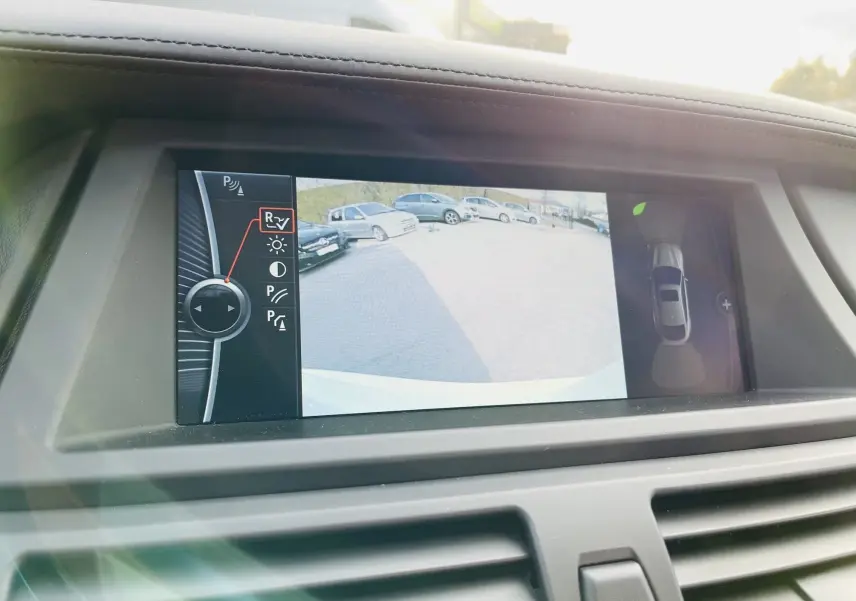 Écran intérieur du BMW X6 blanc montrant la caméra de recul avec vue Top View et commandes du système d'aide au stationnement.