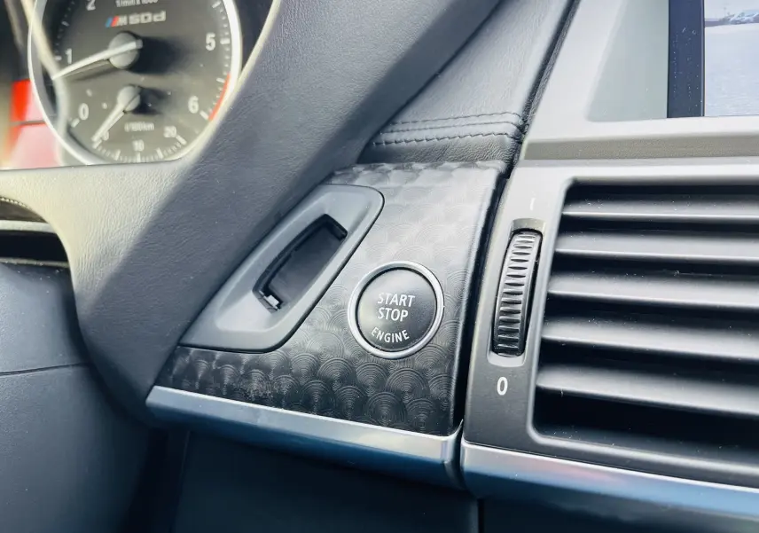 Gros plan sur le bouton Start/Stop moteur et tableau de bord noir du BMW X6 50D blanc, intérieur moderne et soigné.