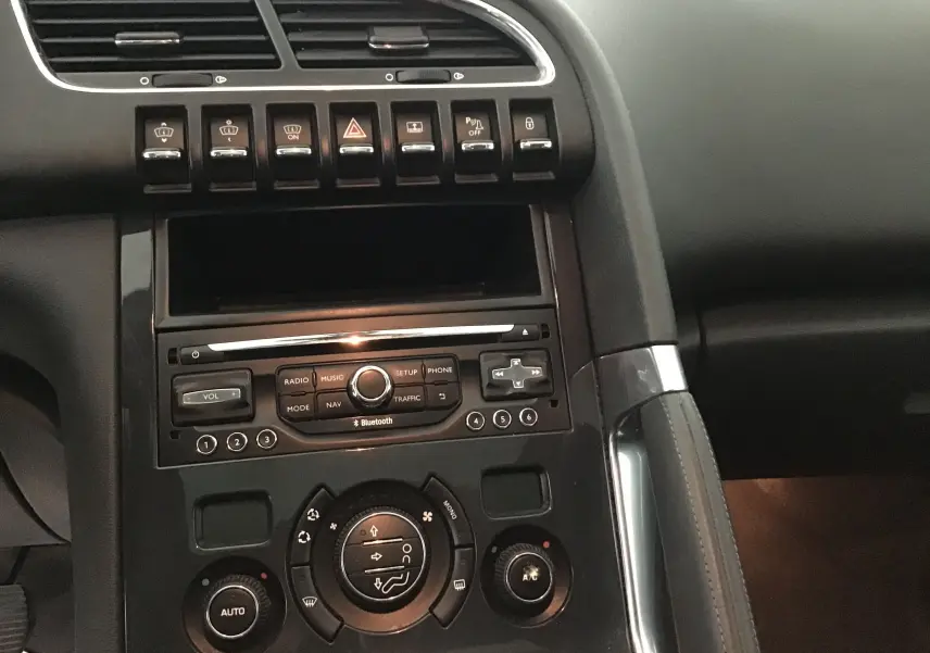 Vue rapprochée de la console centrale noire du Peugeot 3008 blanc, avec commandes de climatisation et radio Bluetooth visibles.