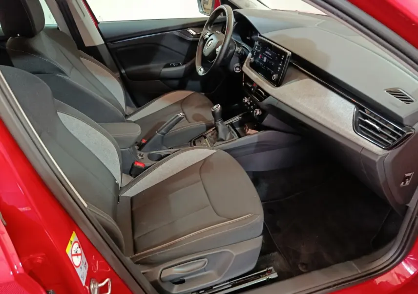 Intérieur côté conducteur d’une Skoda Kamiq rouge 2024, montrant sièges tissu bicolore et tableau de bord avec écran tactile.
