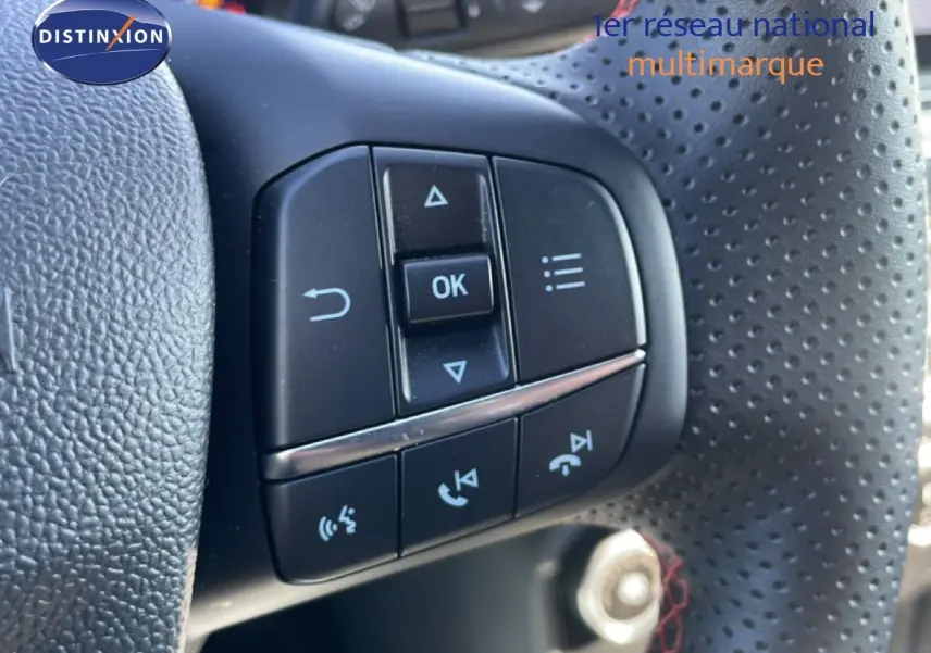 Gros plan sur les commandes multifonctions noires du volant perforé côté gauche d’un Ford Puma gris Solar Metal.