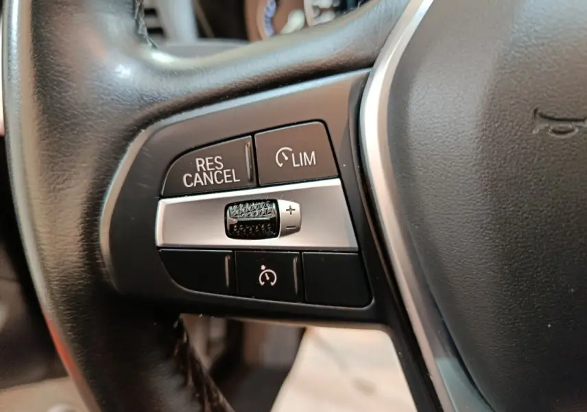 Gros plan sur les commandes de régulateur de vitesse et limiteur sur le volant cuir noir du BMW X3 xDrive30e gris foncé.