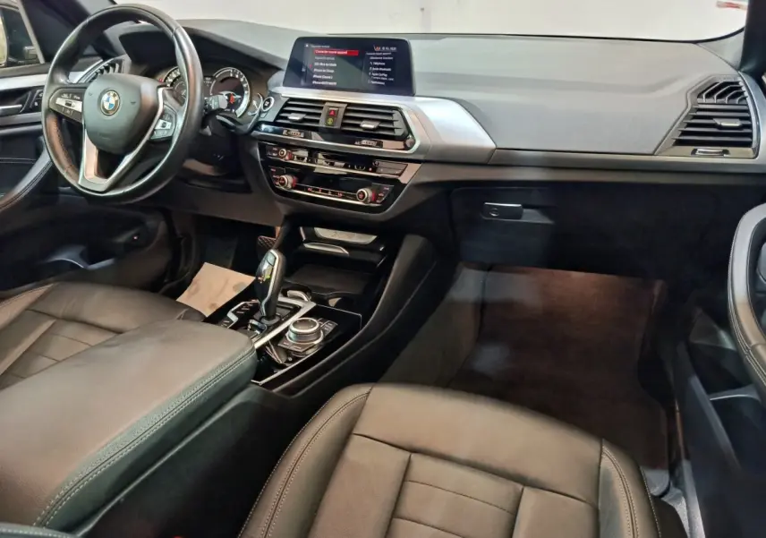 Intérieur BMW X3 xDrive30e 2020 vu côté passager, tableau de bord noir avec écran central et volant cuir multifonctions.