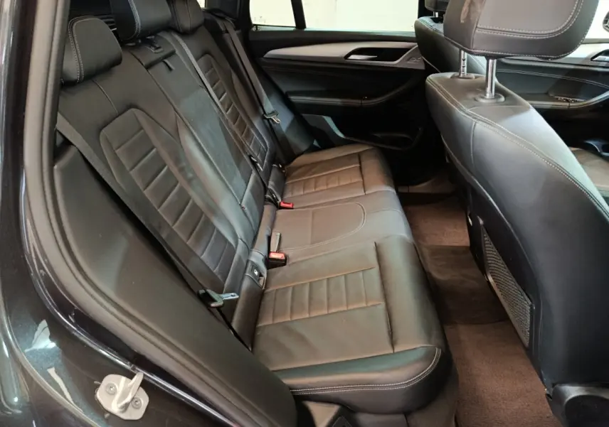 Vue intérieure côté gauche des sièges arrière en cuir noir du BMW X3 xDrive30e gris foncé, avec détails de couture apparents.
