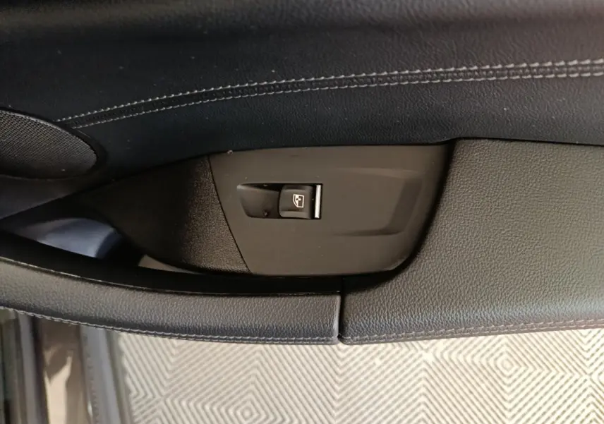 Détail du bouton de commande de vitre sur la porte intérieure noire d’un BMW X3 xDrive30e gris foncé.