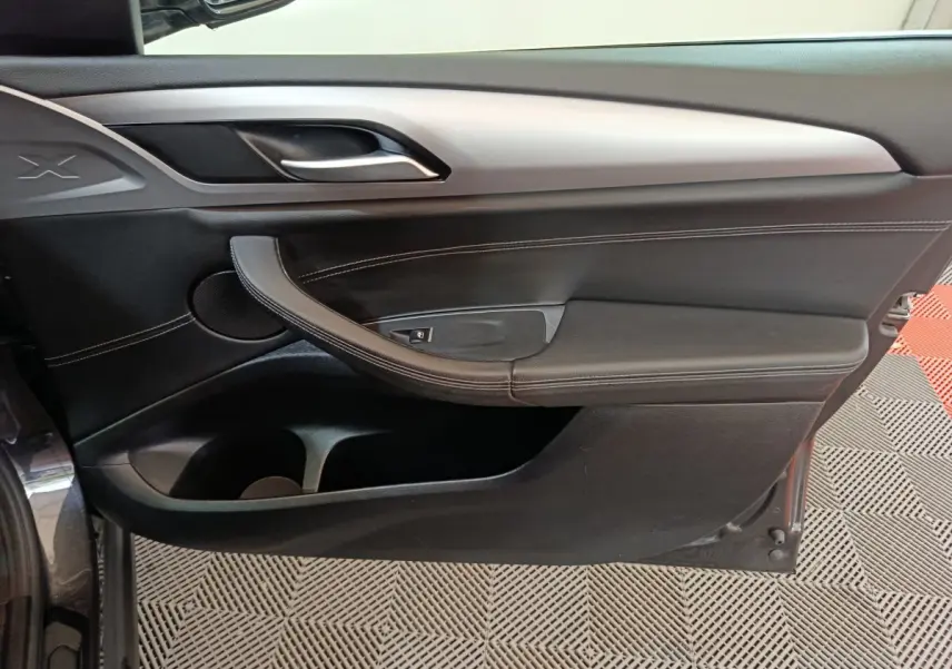 Vue latérale du panneau de porte intérieur droit noir avec poignée argentée et surpiqûres blanches du BMW X3 xDrive30e 2020.