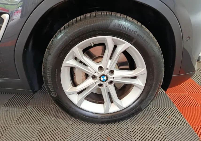 Gros plan sur la roue avant gauche d’un BMW X3 gris foncé, jante alliage argentée et pneu hiver Continental.