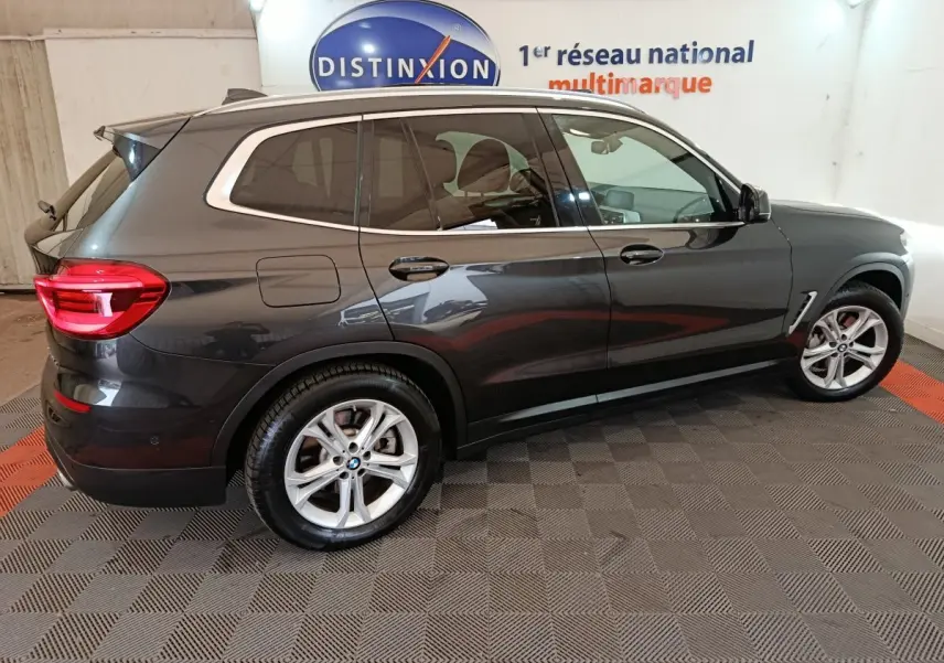 BMW X3 xDrive30e gris foncé vue de profil côté droit, avec jantes alliage et feux arrière allumés dans un showroom.