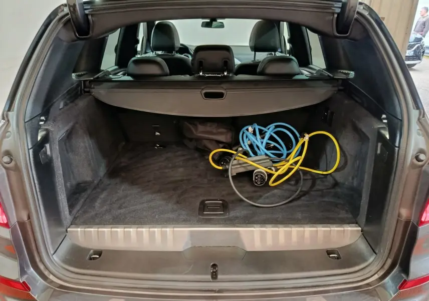 Vue arrière du coffre ouvert d'un BMW X3 gris foncé avec câbles de recharge hybrides visibles à l'intérieur.