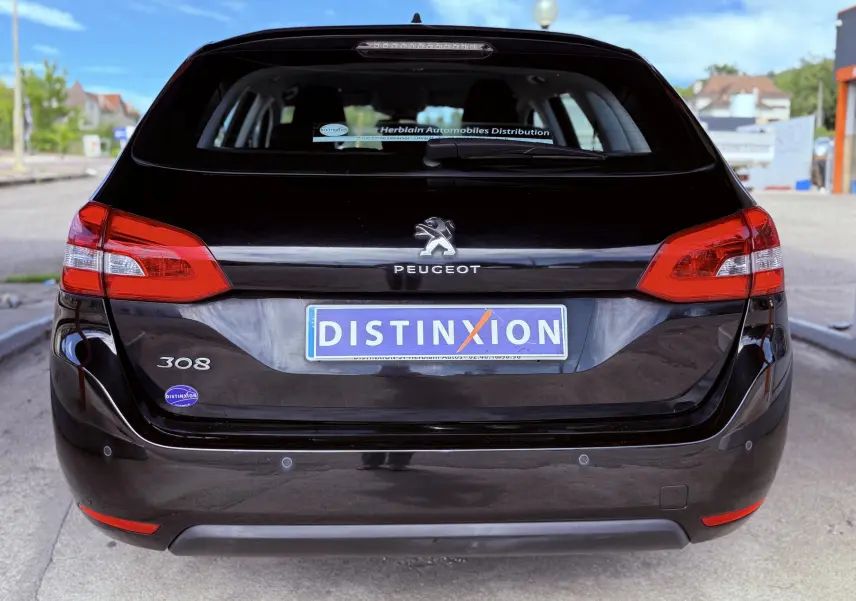 Vue arrière d'une Peugeot 308 SW noire métallisée avec feux rouges et logo distinctif sur le hayon.