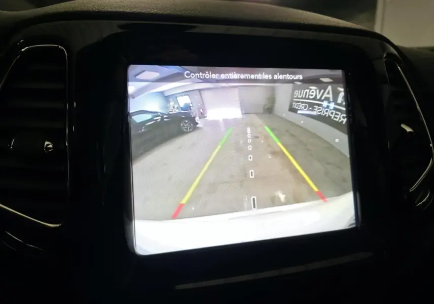 Écran central affichant la caméra de recul du Jeep Compass blanc, avec lignes de guidage colorées en parking intérieur.