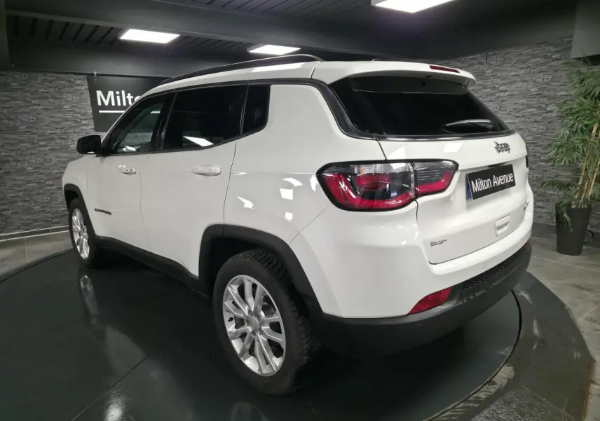 Vue 3/4 arrière droite d'un Jeep Compass blanc avec vitres surteintées et jantes alliage 18 pouces en intérieur showroom.