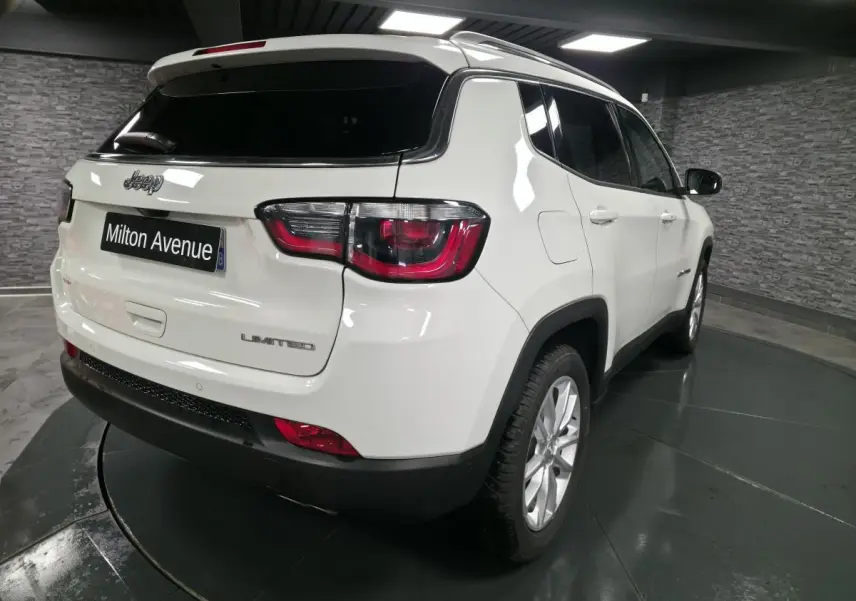 Vue 3/4 arrière droite d'un Jeep Compass blanc avec vitres surteintées et jantes alliage 18 pouces dans un showroom.