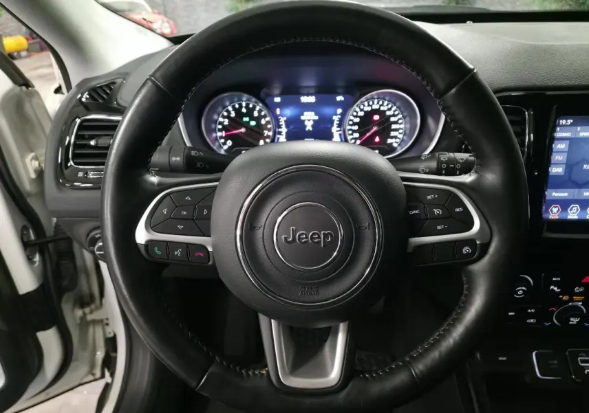 Vue rapprochée du volant en cuir noir du Jeep Compass 2020 avec tableau de bord et écran tactile visibles.