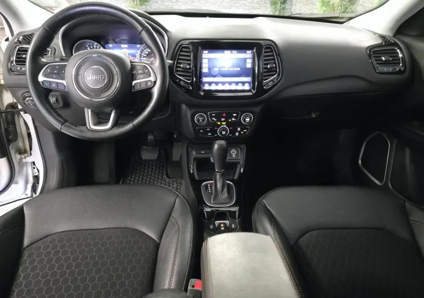 Vue intérieure avant du Jeep Compass 2020 avec volant cuir, écran tactile central et sièges simili cuir noirs.