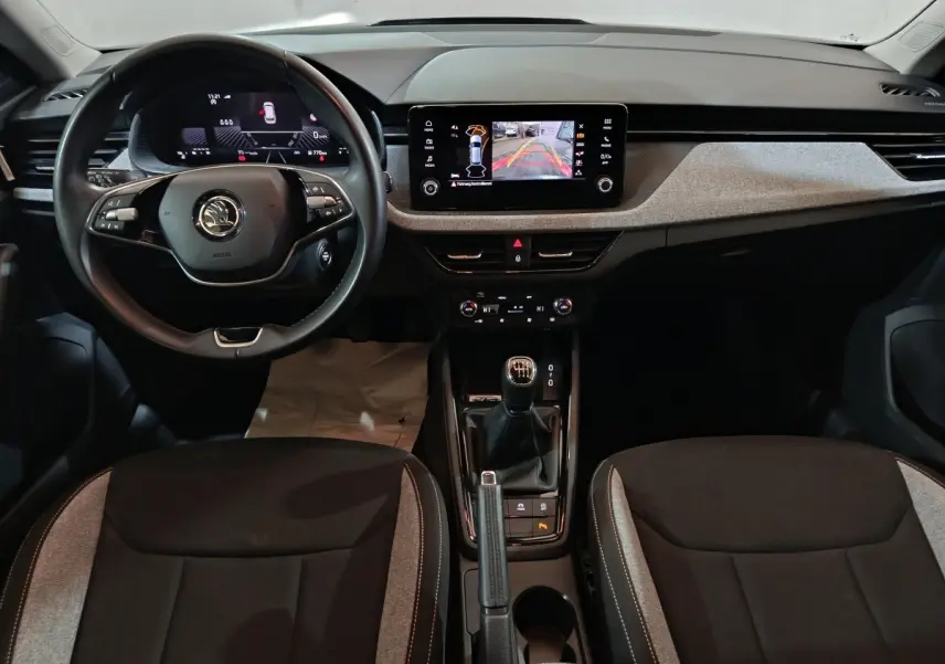 Vue intérieure frontale du tableau de bord et volant cuir noir du Skoda Kamiq 2024 avec écran tactile central et boîte manuelle.