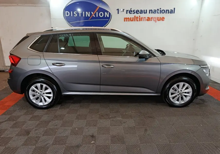 Vue de profil côté gauche d'un Skoda Kamiq gris clair 2024 dans un showroom avec toit ouvrant et jantes alliage.