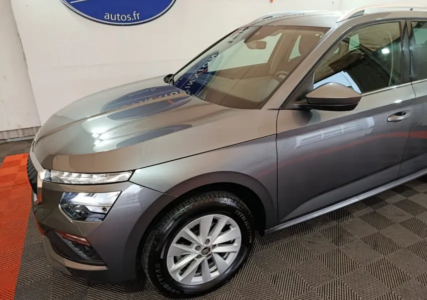 Vue 3/4 avant droit d'un Skoda Kamiq gris clair avec phares LED et jantes alliage en intérieur showroom.