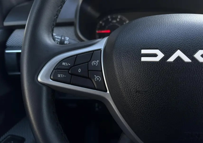 Gros plan sur le volant noir du Dacia Jogger 2025, avec commandes de régulateur de vitesse et logo DACIA visible.
