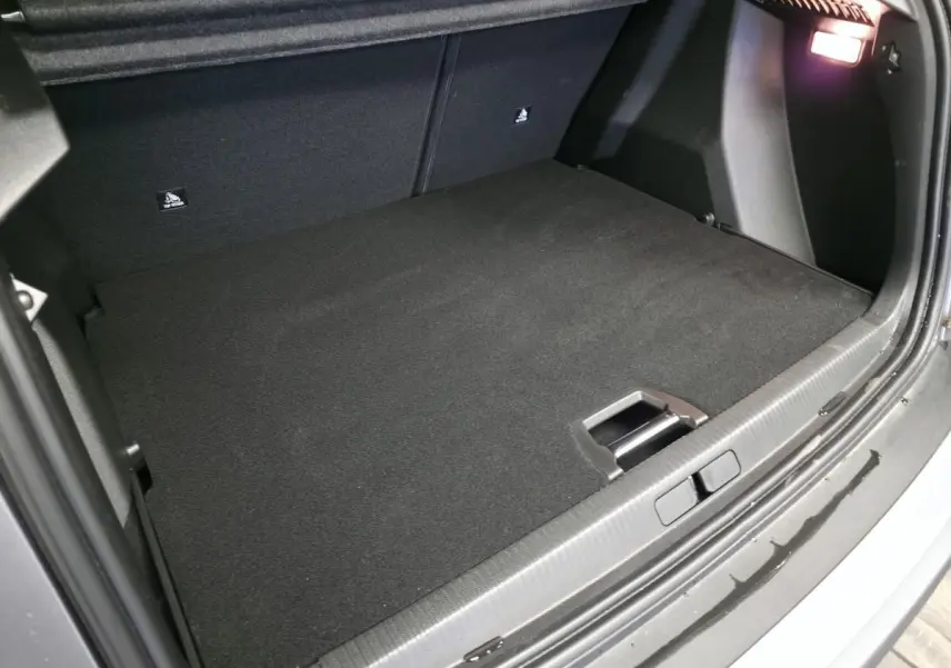 Coffre ouvert vu de l'arrière d'un Peugeot 2008 gris 2025, avec tapis noir et éclairage intérieur allumé.