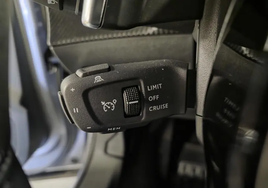 Gros plan sur la commande de régulateur de vitesse noir à gauche du volant dans le Peugeot 2008 gris 2025.