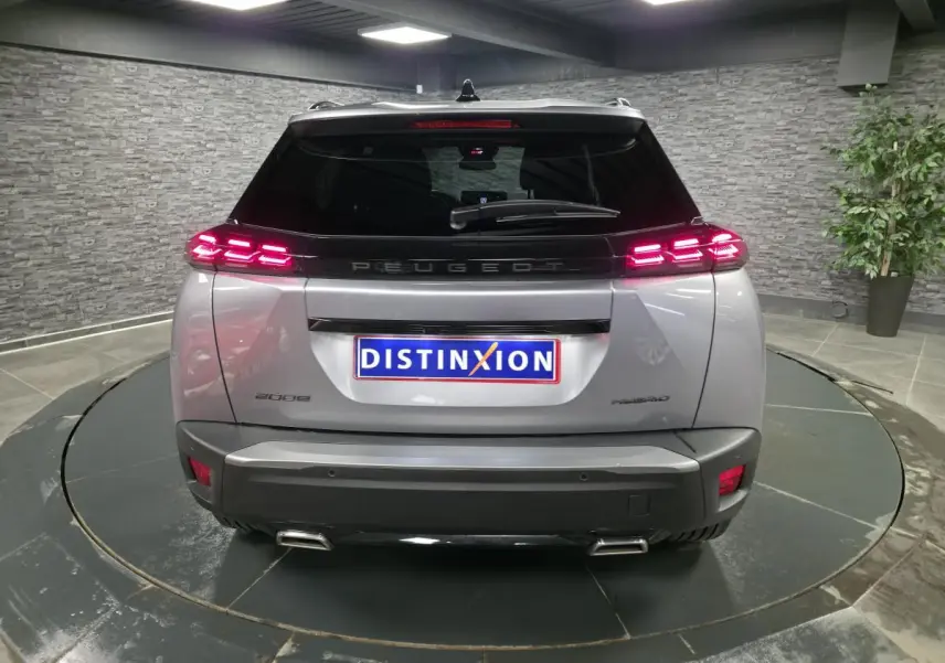 Vue arrière d'un Peugeot 2008 gris avec feux LED allumés et double canule d'échappement chromée dans un showroom.