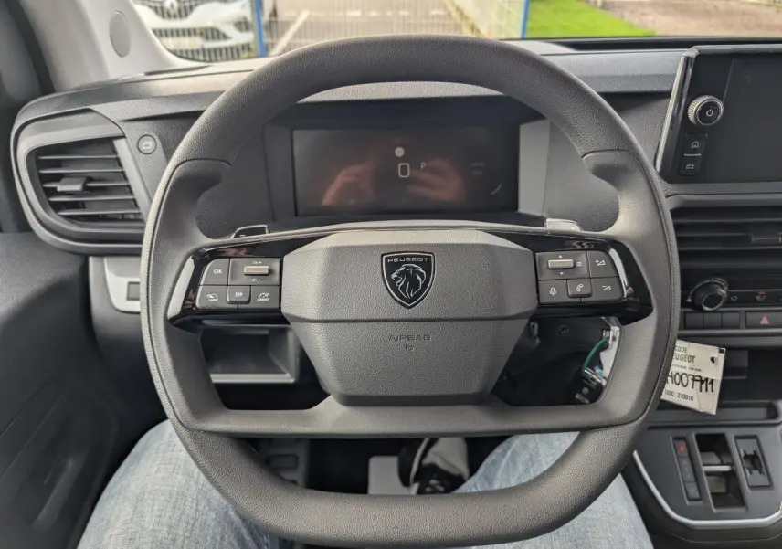Vue rapprochée du volant noir du Peugeot Expert Fourgon 2025 avec commandes intégrées et combiné numérique en arrière-plan.
