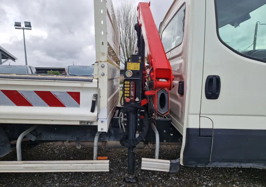 Vue latérale droite d’un Iveco Daily blanc avec benne et grue rouge Palfinger déployée entre cabine et plateau.
