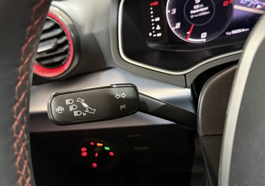 Gros plan sur la manette de clignotants noire avec marquages blancs, volant cuir rouge et tableau de bord digital d'une SEAT Ibiza blanche.