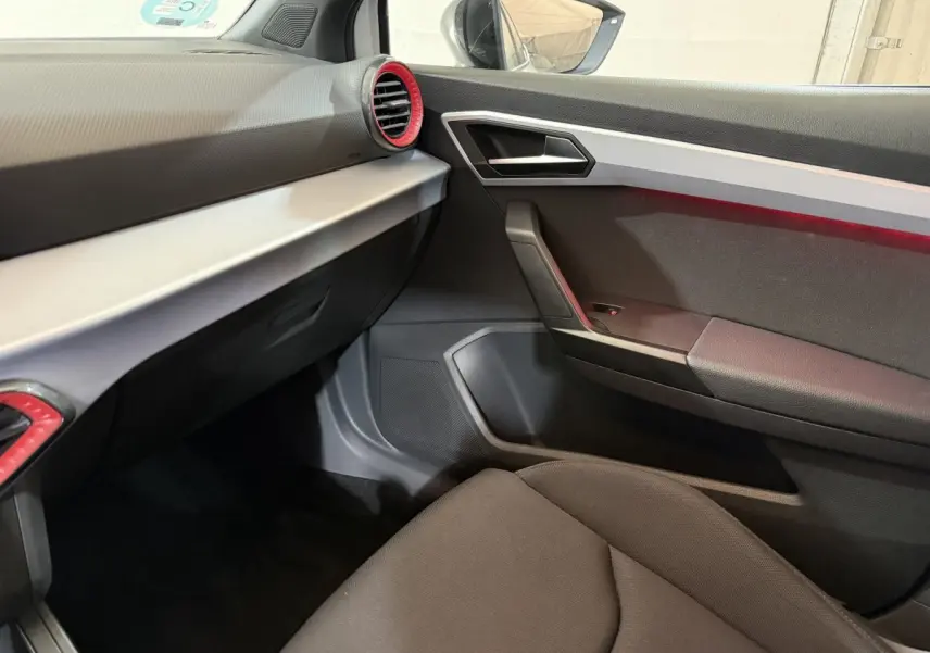 Vue intérieure côté passager de la SEAT Ibiza 2024, avec tableau de bord noir et inserts rouges autour des aérateurs.