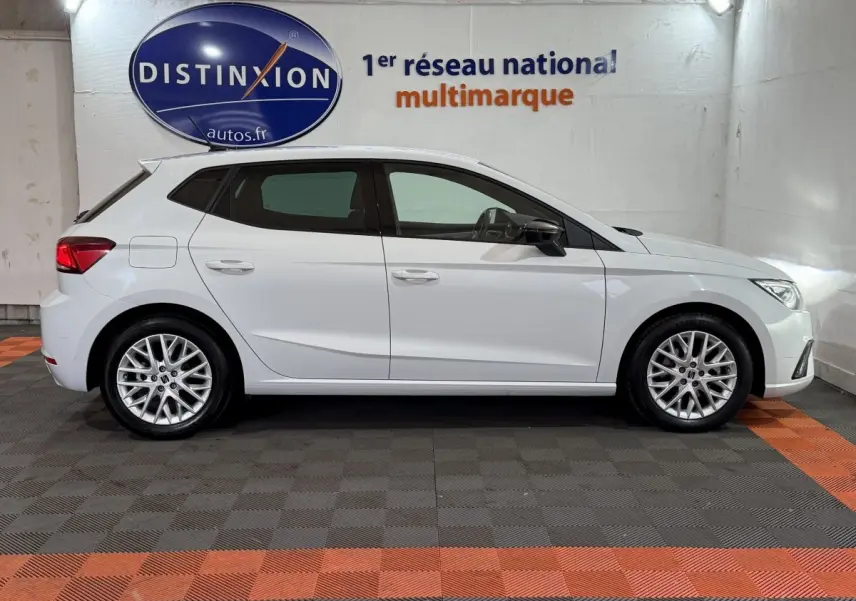 Vue de profil côté gauche d'une SEAT Ibiza 1.0 TSI 110 FR blanche avec jantes alliage multibranches en intérieur showroom.