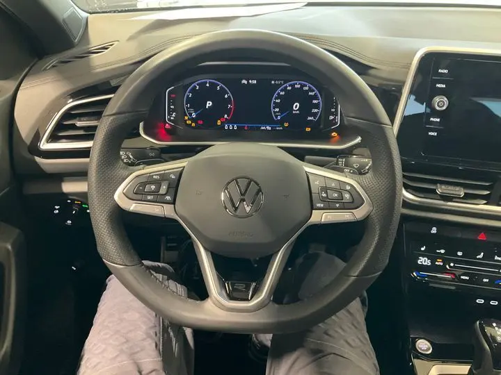 Vue intérieure centrée sur le volant noir du Volkswagen T-Roc 2025 avec tableau de bord digital et console tactile.