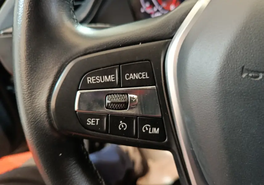 Gros plan sur les commandes de régulateur de vitesse au volant cuir noir de la BMW Série 1 118i Edition Sport 2023.