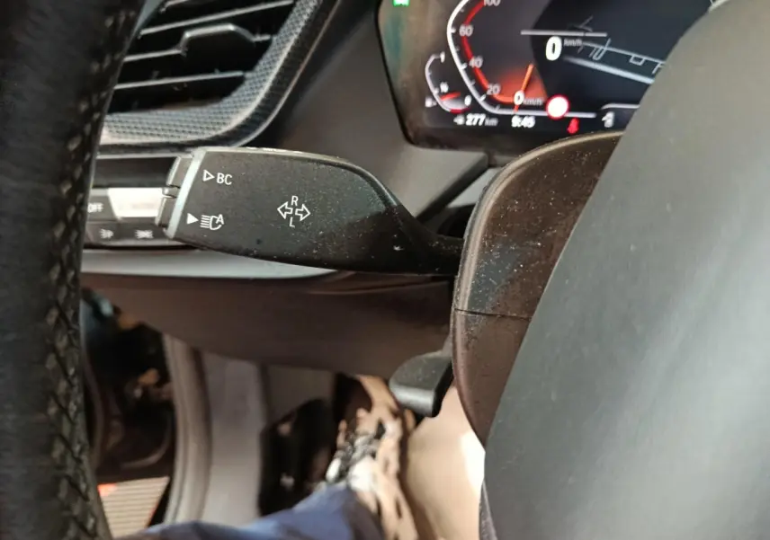Gros plan sur la manette de clignotant gauche et le tableau de bord numérique d'une BMW Série 1 118i noire de 2023.