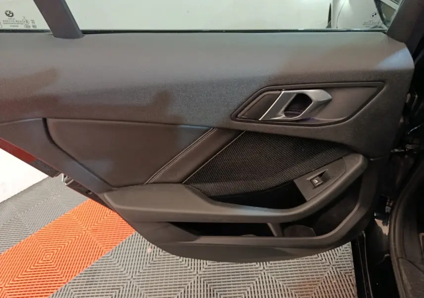 Vue intérieure du panneau de porte côté gauche noir de la BMW Série 1 118i Edition Sport 2023 avec poignée et commande de vitre.