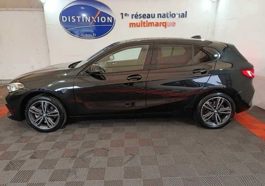 BMW Série 1 118i Edition Sport noire vue de profil côté gauche, avec jantes alliage et feux arrière LED allumés.