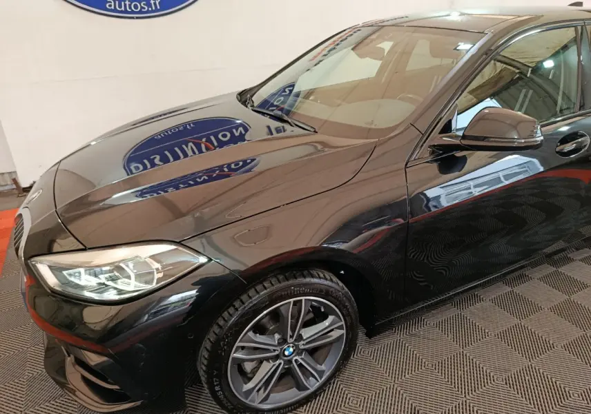 BMW Série 1 118i Edition Sport noire vue 3/4 avant droit, avec phares LED et jantes alliage visibles.