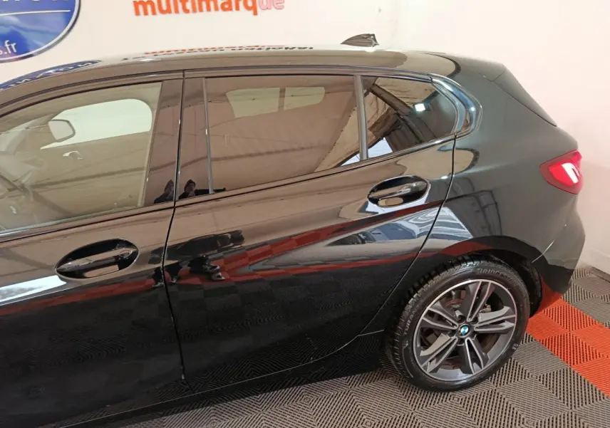 Vue latérale côté gauche d'une BMW Série 1 noire, mettant en valeur la porte arrière et la roue arrière alliage.