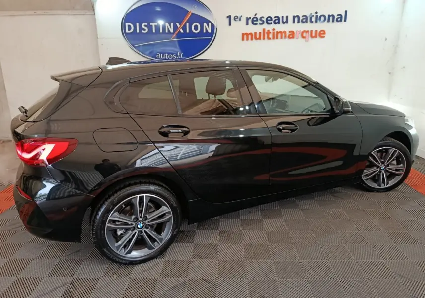 BMW Série 1 118i Edition Sport noire vue de profil côté gauche, avec jantes alliage et feux arrière LED allumés.