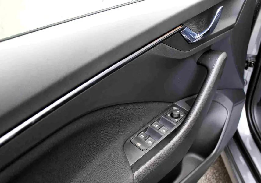 Gros plan sur la porte avant gauche du Skoda Kamiq gris graphite, montrant les commandes des vitres et la poignée intérieure chromée.