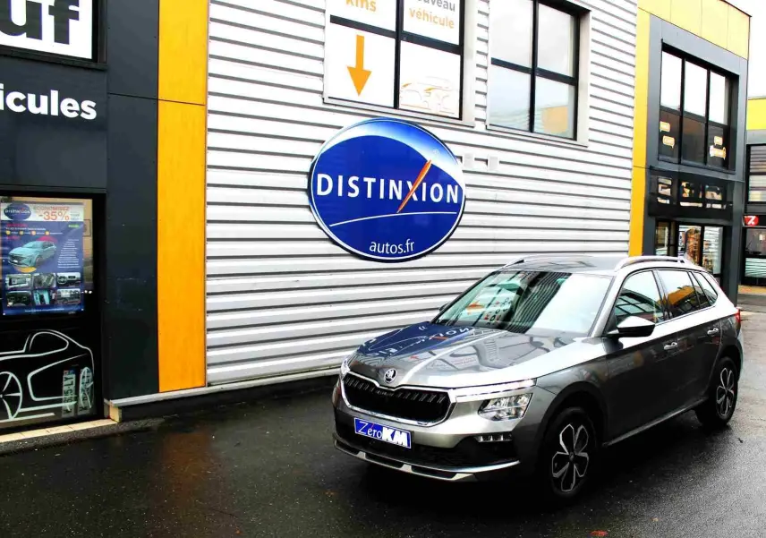 Vue 3/4 avant droite d'un Skoda Kamiq gris graphite avec calandre noire et jantes bi-ton devant un mur métallique.