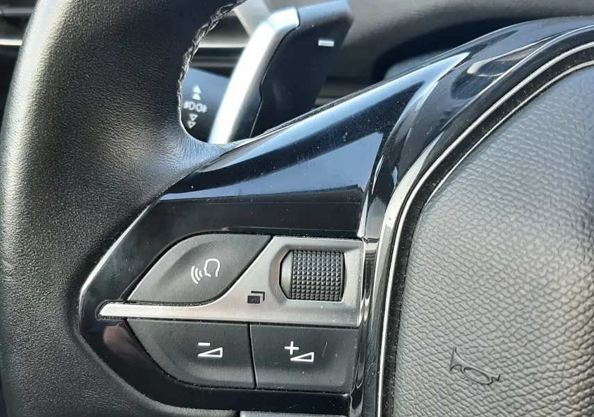 Gros plan sur les commandes gauche du volant noir du Peugeot 3008 gris Amazonite, avec molette et boutons de volume.